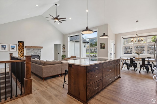 kitchen with high vaulted ceiling, a chandelier, a ceiling fan, light wood-style flooring, and a fireplace