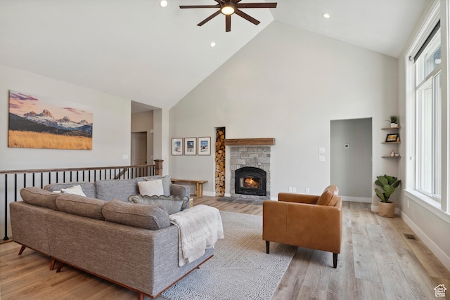 living room featuring high vaulted ceiling, ceiling fan, light wood finished floors, a stone fireplace, and recessed lighting