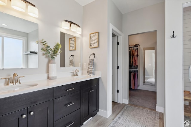 full bathroom featuring wood finished floors, a walk in closet, double vanity, and baseboards