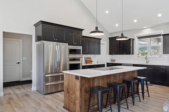 kitchen featuring appliances with stainless steel finishes, backsplash, a kitchen island, a kitchen bar, and light countertops