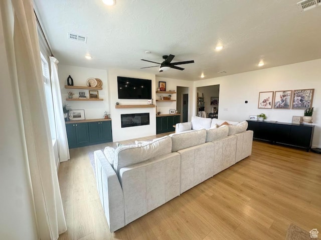 living area with a ceiling fan, light wood finished floors, a glass covered fireplace, recessed lighting, and a textured ceiling