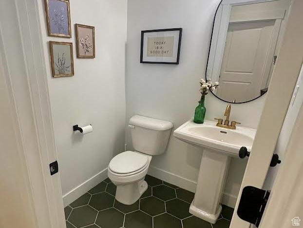 half bath featuring toilet, baseboards, tile patterned flooring, and a sink