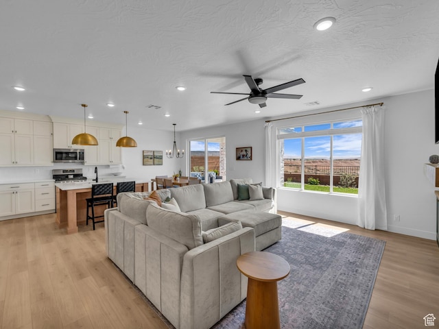 living area with recessed lighting, ceiling fan, light wood-style floors, baseboards, and a chandelier