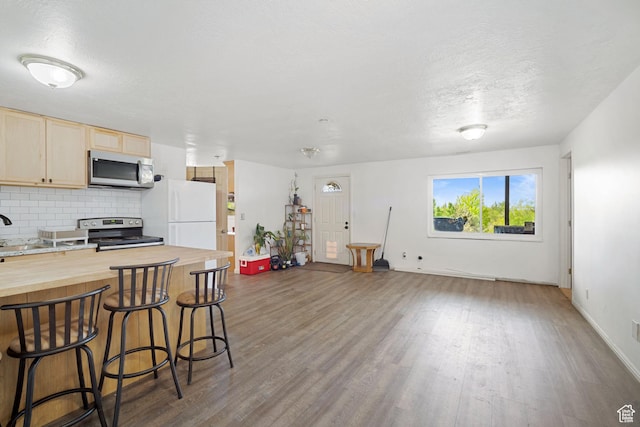kitchen with appliances with stainless steel finishes, butcher block countertops, dark wood-style flooring, a kitchen bar, and a textured ceiling