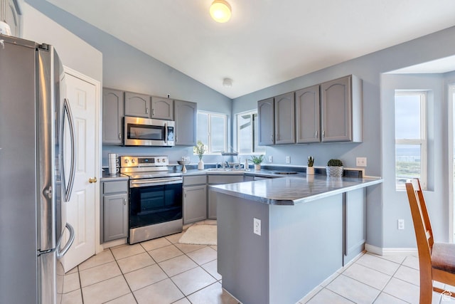 kitchen featuring stainless steel appliances, gray cabinets, a peninsula, lofted ceiling, and light tile patterned flooring
