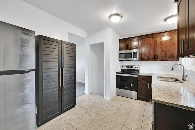 kitchen featuring appliances with stainless steel finishes, a sink, light stone countertops, and decorative backsplash