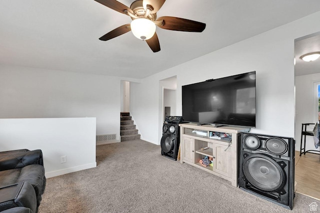 carpeted living room featuring ceiling fan, baseboards, and stairs