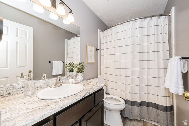 full bathroom with wood finished floors, toilet, vanity, a textured ceiling, and curtained shower