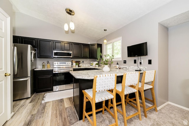 kitchen with stainless steel appliances, lofted ceiling, dark cabinets, hanging light fixtures, and a breakfast bar