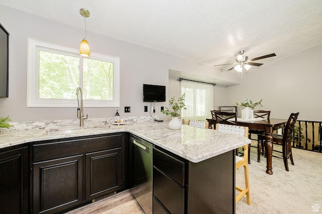 kitchen with a sink, dishwasher, a breakfast bar area, a ceiling fan, and light stone counters