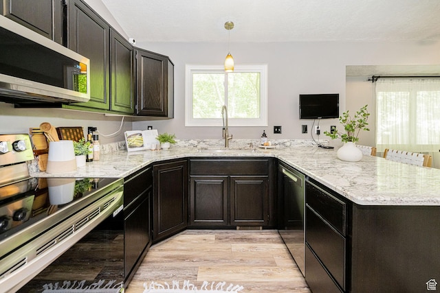kitchen featuring appliances with stainless steel finishes, a sink, light wood-style floors, a peninsula, and light stone countertops