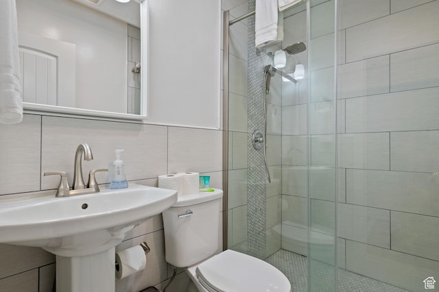 bathroom with a shower stall, toilet, tile walls, tasteful backsplash, and a sink