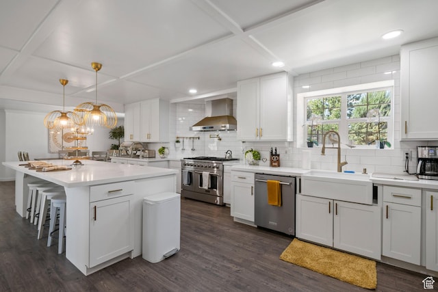 kitchen featuring wall chimney exhaust hood, stainless steel appliances, a sink, coffered ceiling, and backsplash