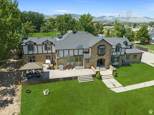 back of house with a gazebo, a mountain view, a yard, a shingled roof, and a patio