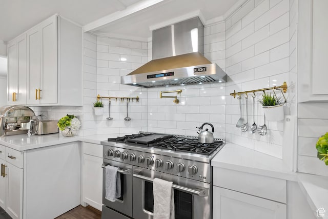 kitchen featuring range with two ovens, wall chimney exhaust hood, backsplash, and light countertops
