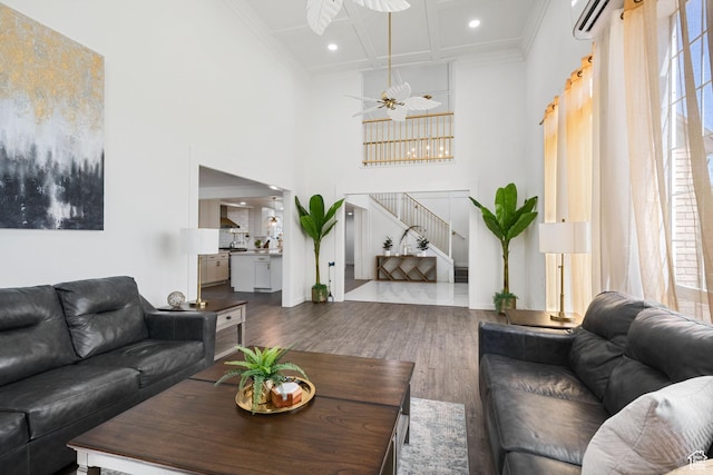 living room with stairway, wood finished floors, a high ceiling, plenty of natural light, and crown molding