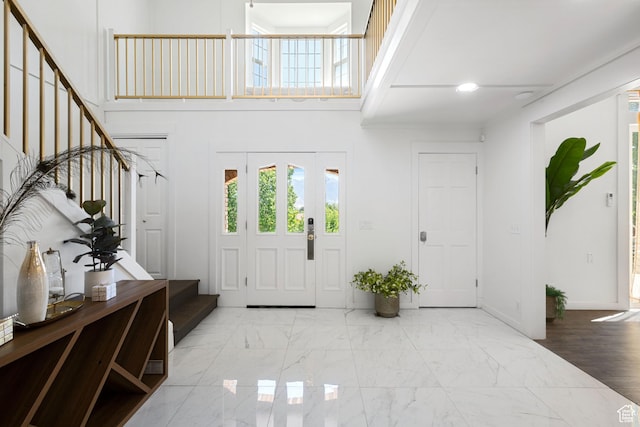 entrance foyer featuring stairs, healthy amount of natural light, a towering ceiling, and marble look tile flooring