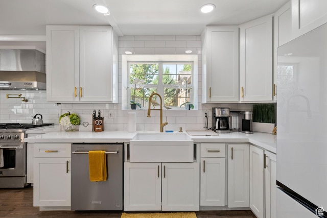 kitchen with stainless steel appliances, wall chimney exhaust hood, a sink, tasteful backsplash, and white cabinetry