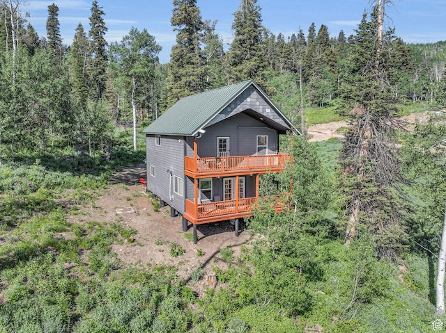 back of property with a forest view, a wooden deck, and metal roof
