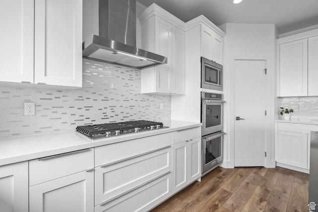 kitchen featuring wall chimney exhaust hood, appliances with stainless steel finishes, decorative backsplash, white cabinetry, and light countertops