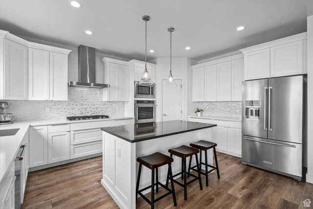 kitchen with appliances with stainless steel finishes, wall chimney exhaust hood, a kitchen island, white cabinets, and recessed lighting