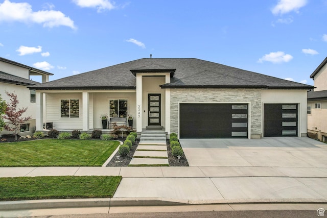 prairie-style house with a garage, driveway, a front lawn, covered porch, and roof with shingles
