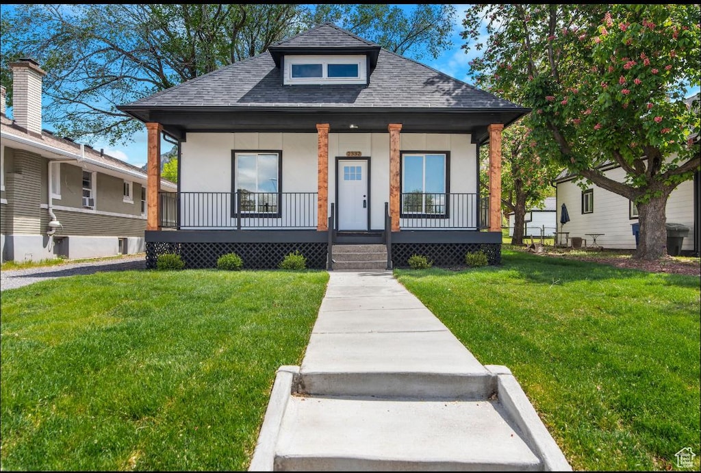 bungalow-style home with a shingled roof, covered porch, stucco siding, and a front yard
