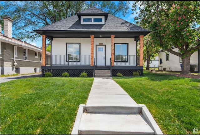 bungalow-style home with a shingled roof, covered porch, stucco siding, and a front yard