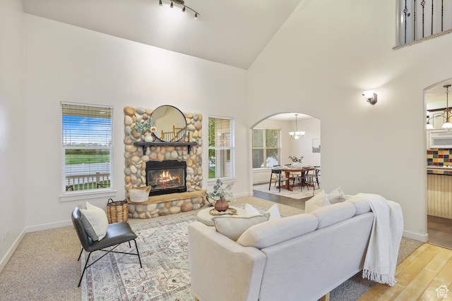 living area featuring plenty of natural light, arched walkways, baseboards, high vaulted ceiling, and a fireplace
