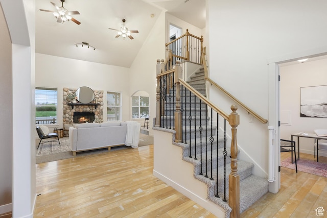 staircase featuring high vaulted ceiling, hardwood / wood-style floors, ceiling fan, a fireplace, and baseboards