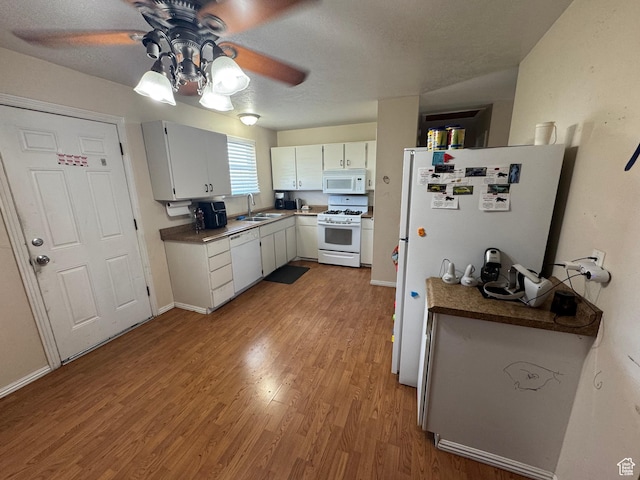 kitchen with white appliances, a sink, ceiling fan, wood finished floors, and baseboards