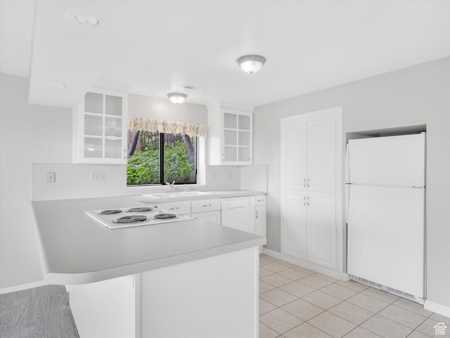 kitchen featuring white appliances, a sink, a peninsula, light countertops, and glass insert cabinets