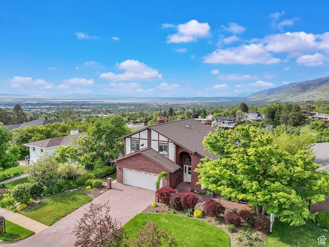 view of front of house featuring driveway, a garage, a shingled roof, a front yard, and a mountain view