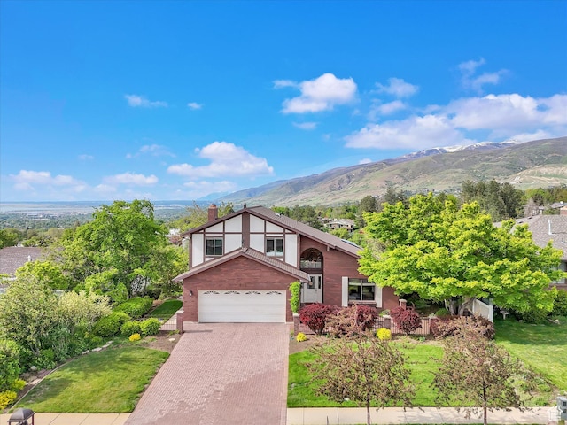 view of front of house with a garage, a mountain view, decorative driveway, a chimney, and a front yard