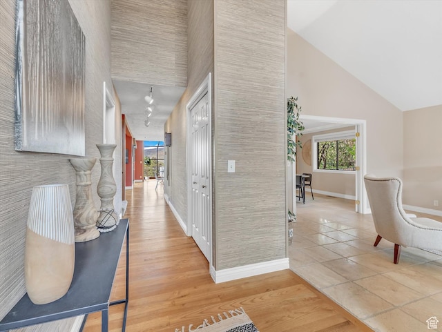 corridor with baseboards, high vaulted ceiling, and light tile patterned floors