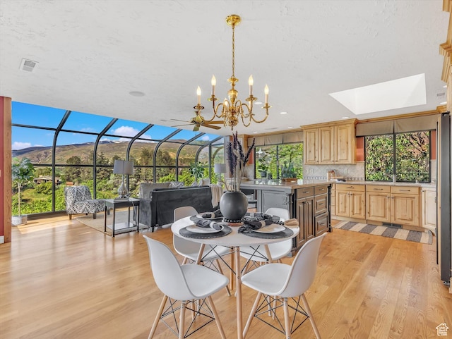 dining area with light wood-style floors, a skylight, and a chandelier