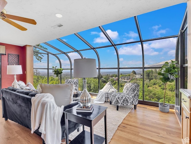 living room featuring a sunroom, a ceiling fan, healthy amount of natural light, wood finished floors, and a wall of windows