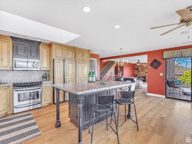 kitchen featuring stainless steel appliances, ceiling fan, a kitchen bar, light wood finished floors, and recessed lighting