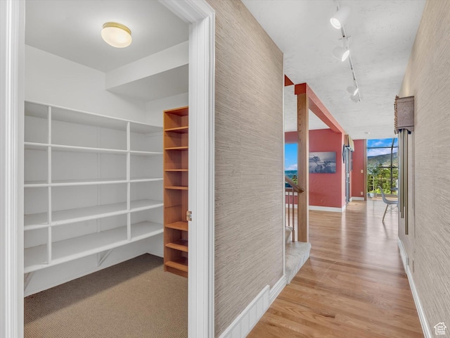 hall featuring rail lighting, wood finished floors, and baseboards