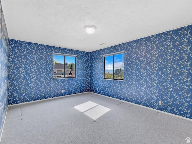 carpeted spare room with wallpapered walls and a textured ceiling