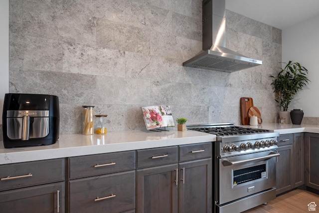 kitchen featuring wall chimney exhaust hood, high end range, light countertops, and tasteful backsplash