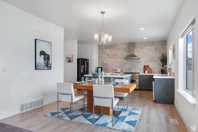 kitchen with wall chimney exhaust hood, high end range, a sink, light countertops, and black refrigerator with ice dispenser