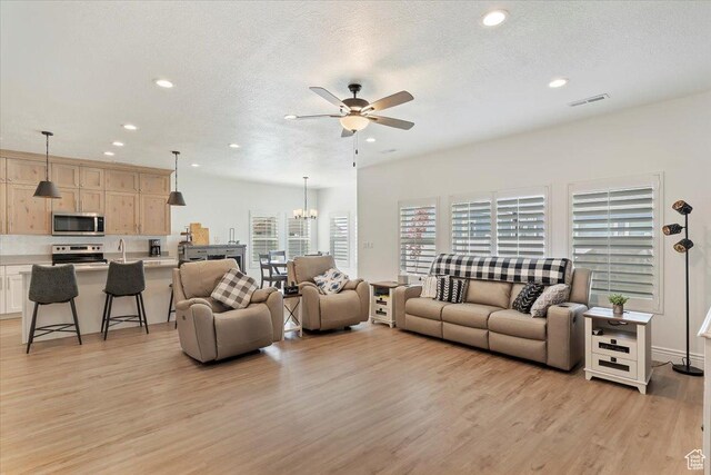 living area featuring ceiling fan, light wood-type flooring, recessed lighting, a chandelier, and a textured ceiling