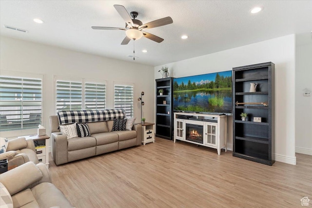 living area with wood finished floors, ceiling fan, recessed lighting, a glass covered fireplace, and baseboards