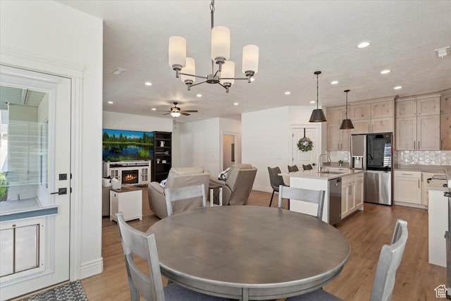 dining room with ceiling fan, a chandelier, wood finished floors, recessed lighting, and a warm lit fireplace