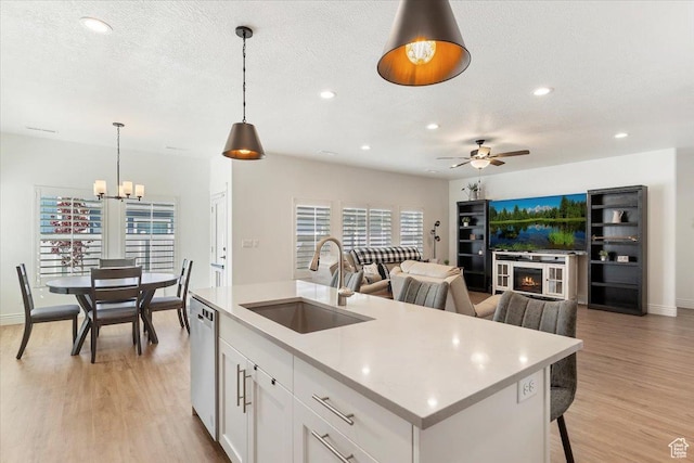 kitchen featuring a sink, light countertops, a ceiling fan, light wood finished floors, and a kitchen island with sink
