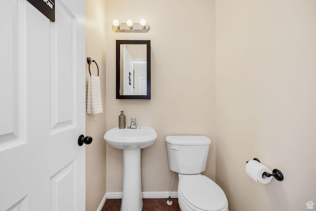 half bath with toilet, baseboards, tile patterned flooring, and a sink