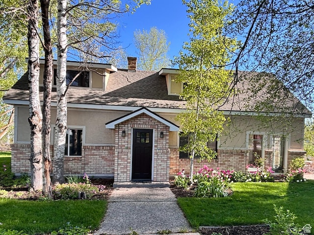 view of front of house with brick siding, stucco siding, a front yard, a chimney, and a shingled roof
