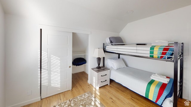 bedroom with vaulted ceiling, light wood-type flooring, and baseboards