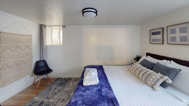 bedroom with wood finished floors, a textured ceiling, and baseboards